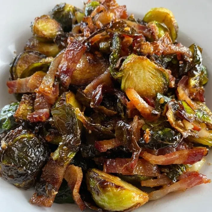 Caramelized Brussels sprouts and crispy bacon in a white dish.