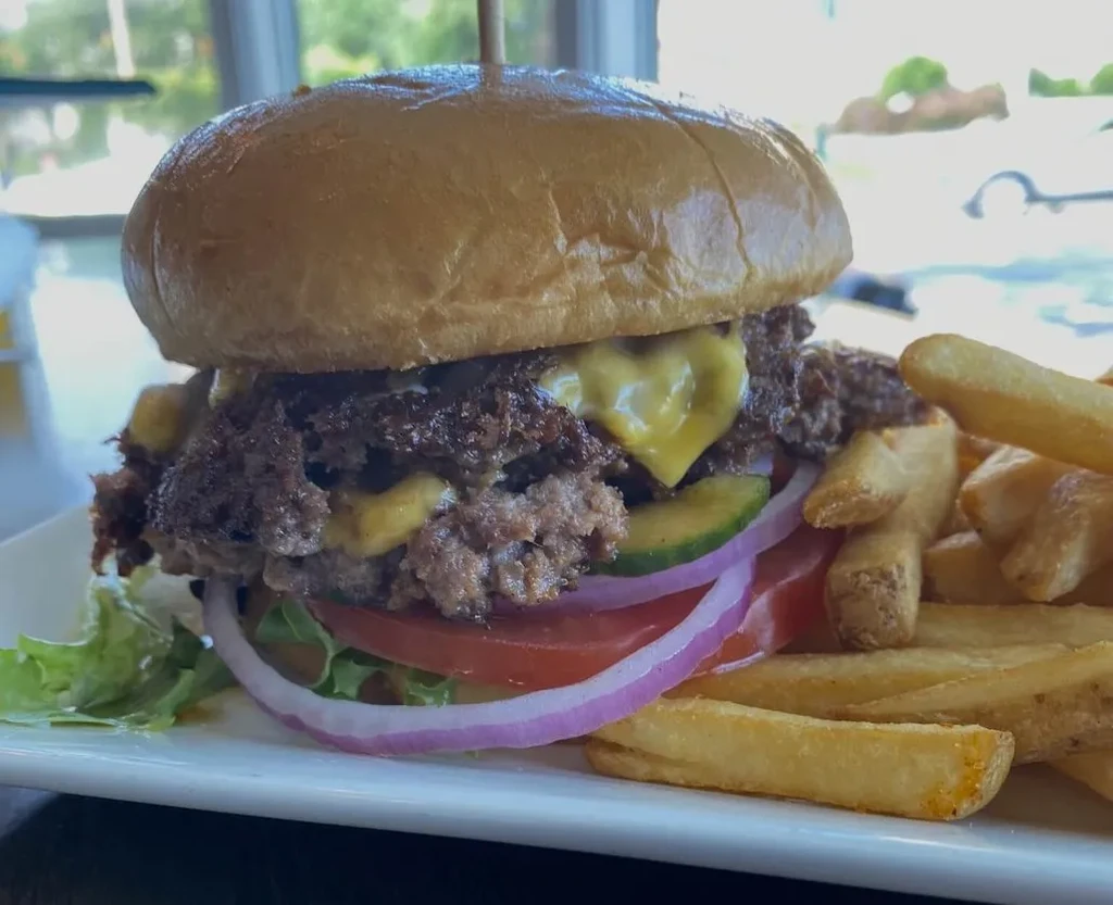 Close-up of a burger with two patties, cheese, vegetables, and fries.