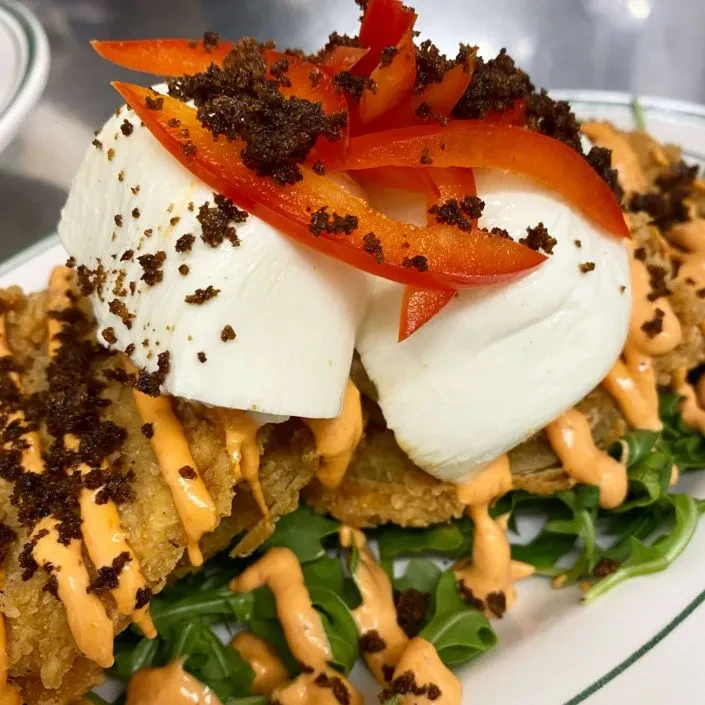Fried appetizer stack with cheese, sauce, peppers, crumbs, and greens.