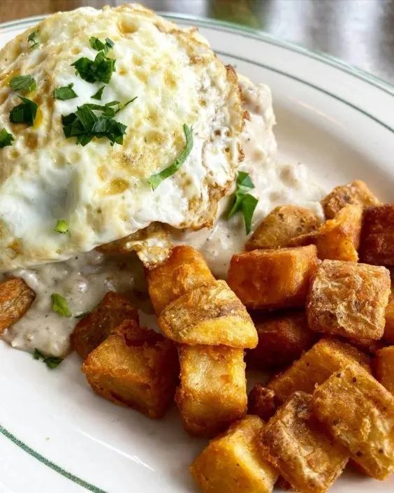 Fried egg topped with herbs, gravy, and crispy home fries.