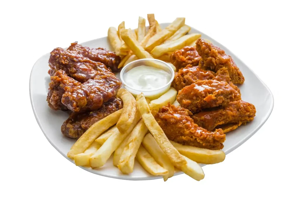 Plate of glazed and crispy chicken wings with fries and dip.