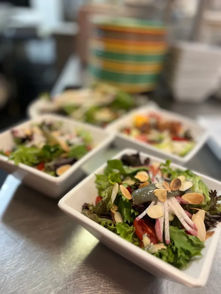 Multiple individual salads with lettuce, tomatoes, radishes, and almonds in white bowls.