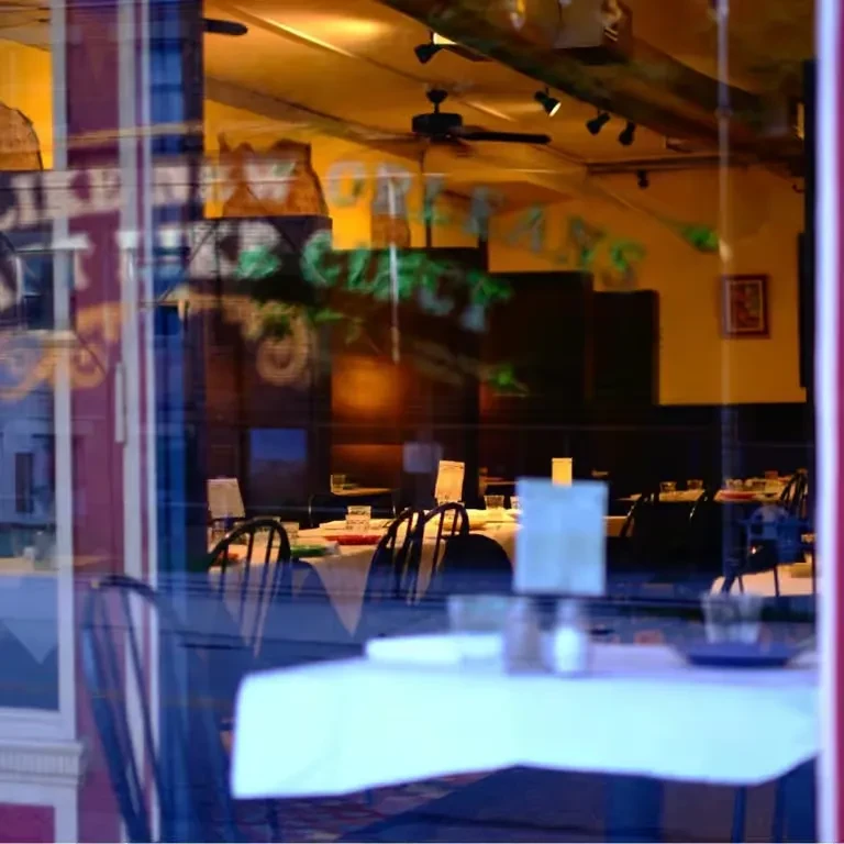 Empty restaurant interior: yellow walls, set tables, visible through reflective window.