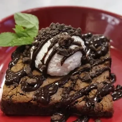 Square chocolate brownie with white ice cream, chocolate sauce, cookie crumbs, mint.