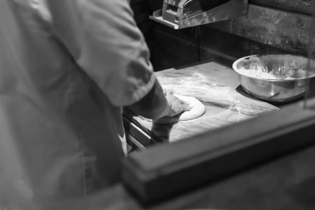 Black and white photo of chef's hands preparing dough on floured surface.