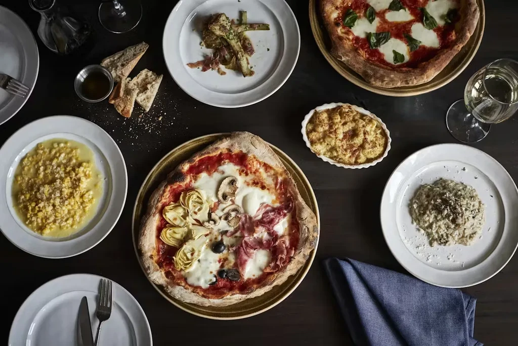 Overhead shot of Italian pizzas, risotto, and other dishes on a dark table.