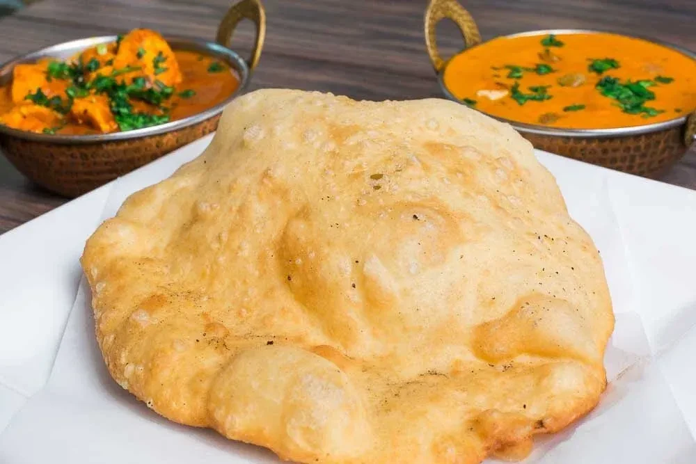 Puffed golden fried bread with paneer curry and another.