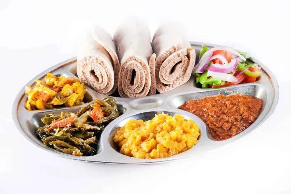Partitioned tray of Ethiopian/Eritrean food: injera, stews, vegetables, salad.
