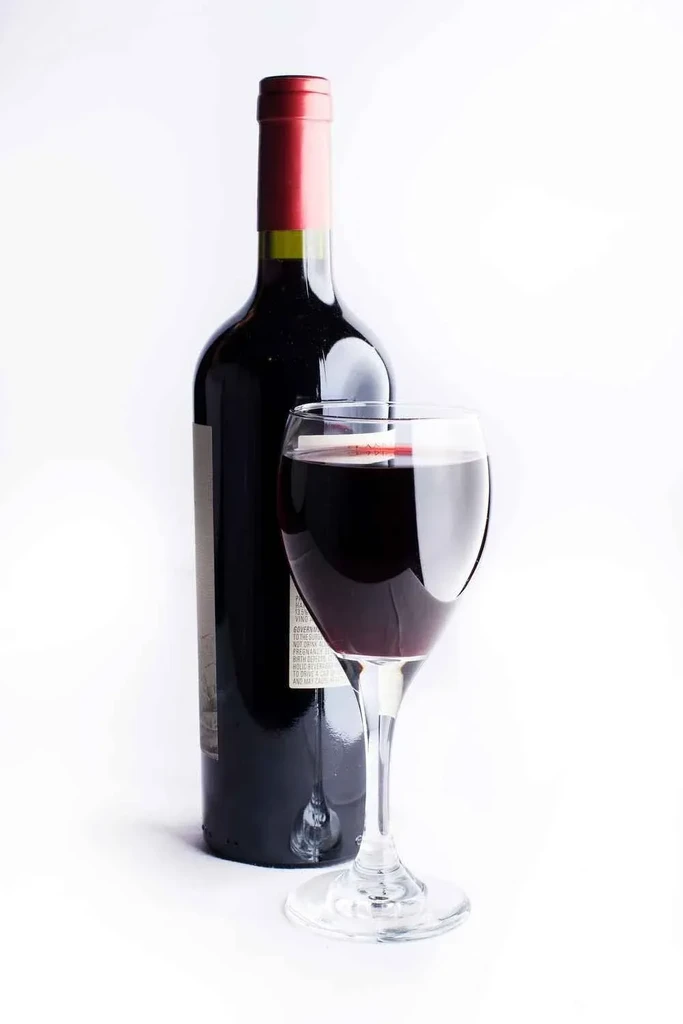 Dark bottle of red wine and glass of red wine on white background.