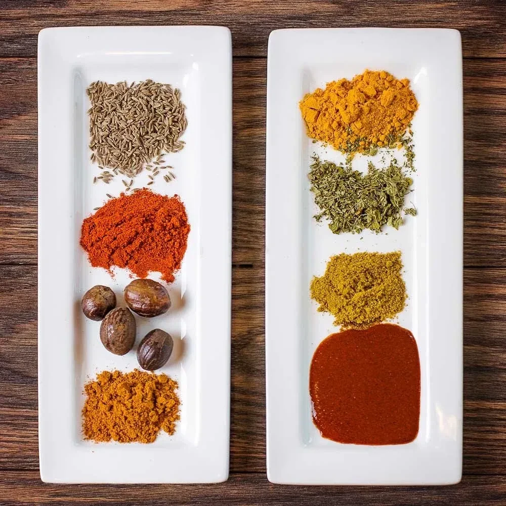 Two white dishes hold neatly arranged spices and ingredients on wood.