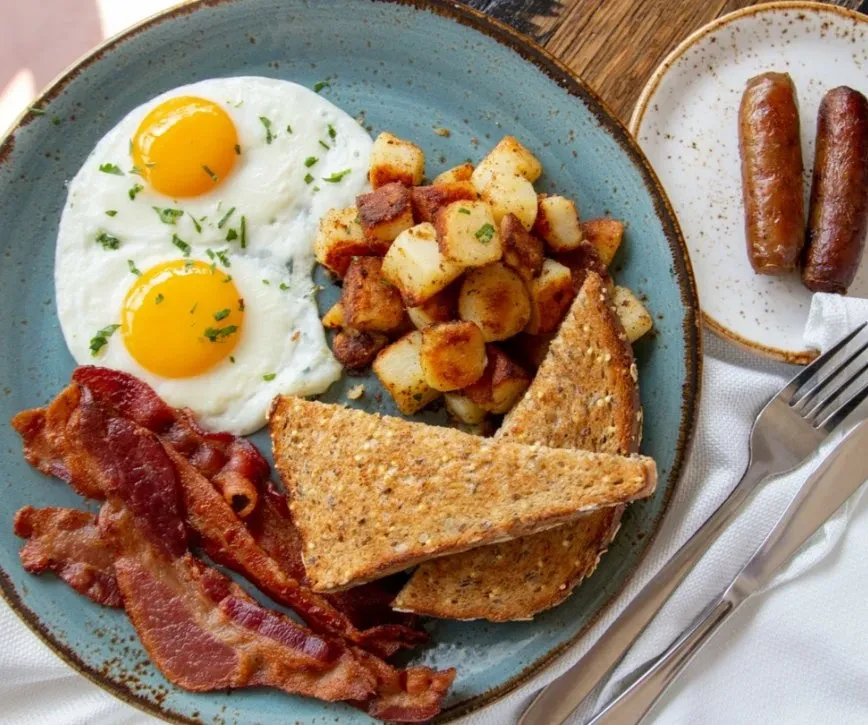 Breakfast platter with fried eggs, bacon, home fries, toast, and sausages.