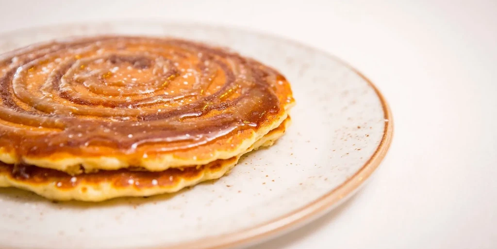 Two golden-brown pancakes stacked with spiral glaze and light specks.