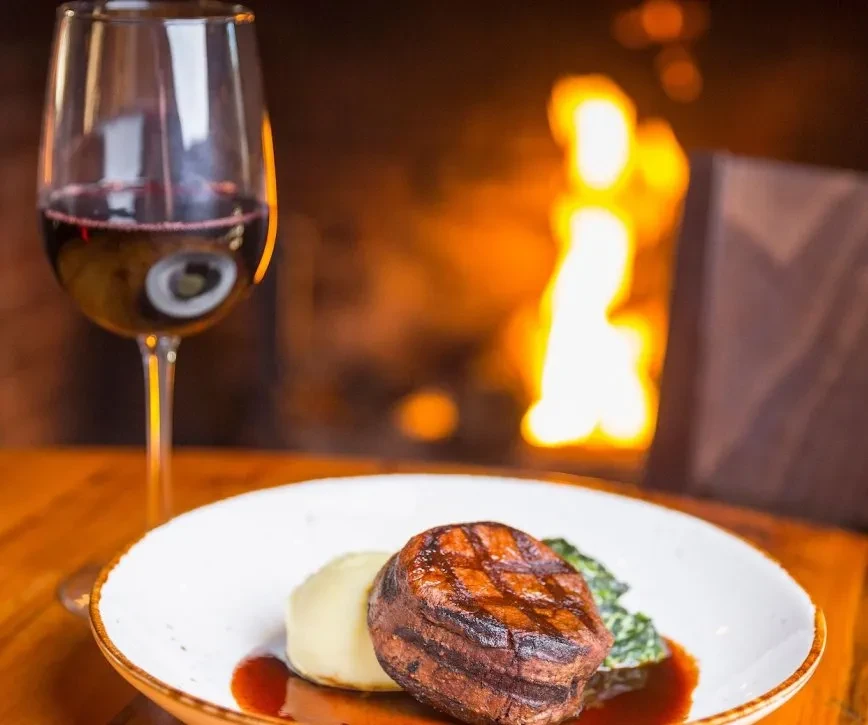 Grilled filet mignon with mashed potatoes, vegetables, red wine by a fireplace.