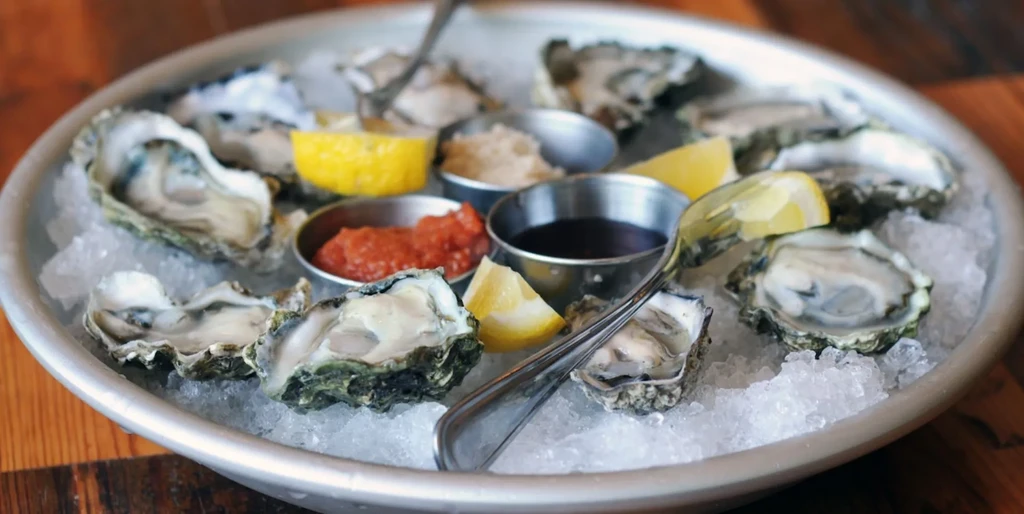 Close-up of shucked oysters on ice with lemon wedges and condiments.