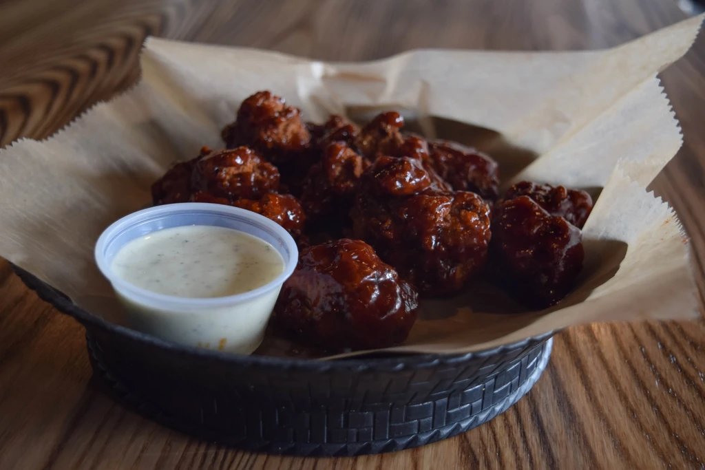 Dark-sauced boneless chicken wings in a basket with creamy dipping sauce.