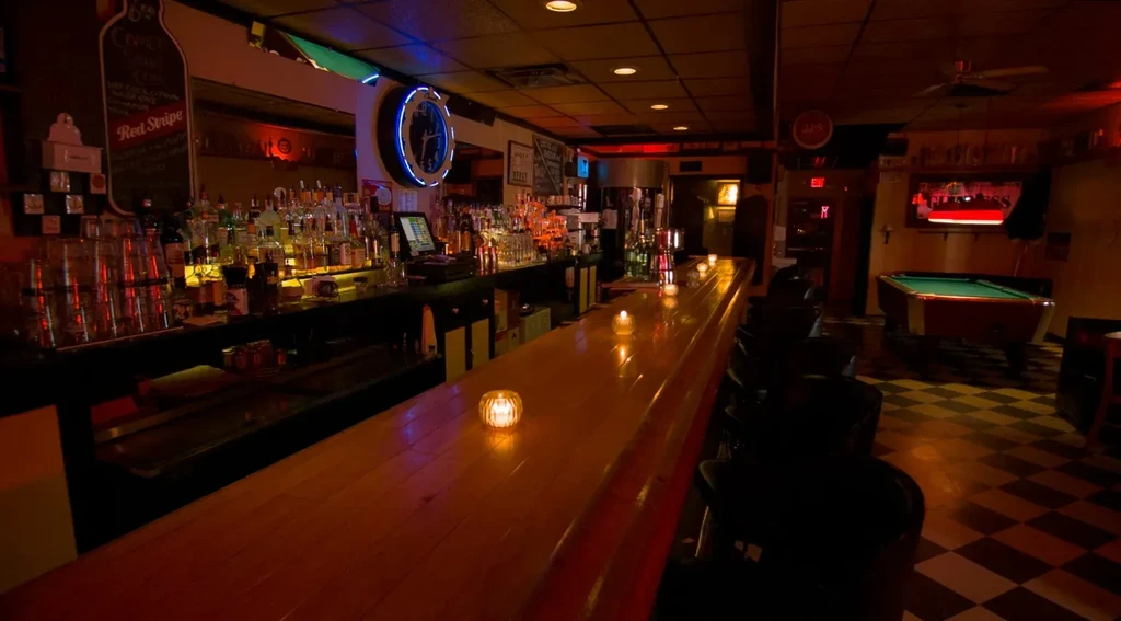 Dimly lit bar with a long wooden counter and glowing liquor display.