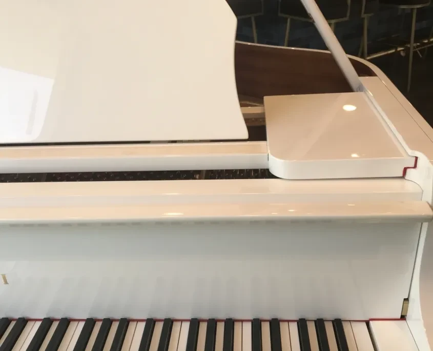 Glossy white grand piano, lid open, showing interior and keys.