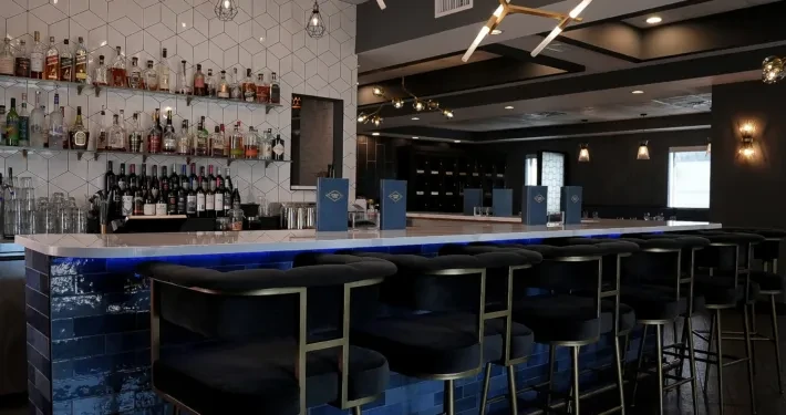 Sleek restaurant bar with blue lighting, black velvet stools, and stocked liquor.