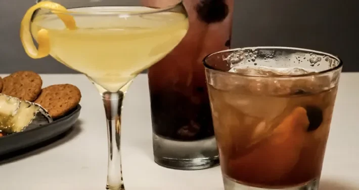 Three cocktails and an appetizer plate on a light surface.