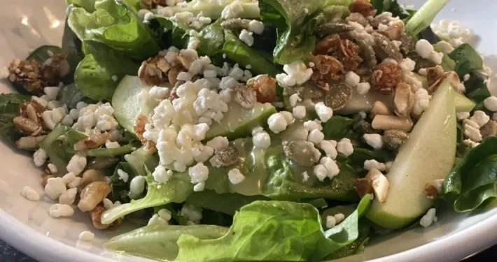 Close-up of vibrant salad with lettuce, cheese, nuts, seeds, and fruit.