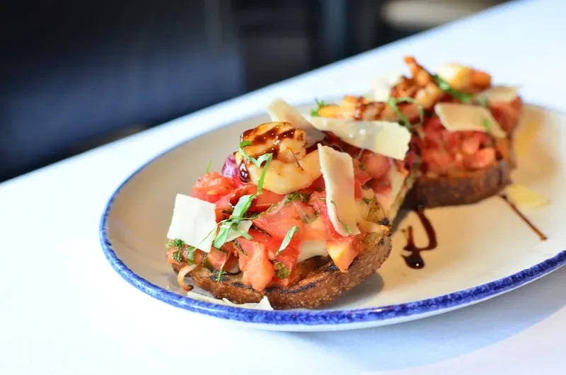 Two bruschetta with grilled shrimp, tomatoes, herbs, cheese, and balsamic.
