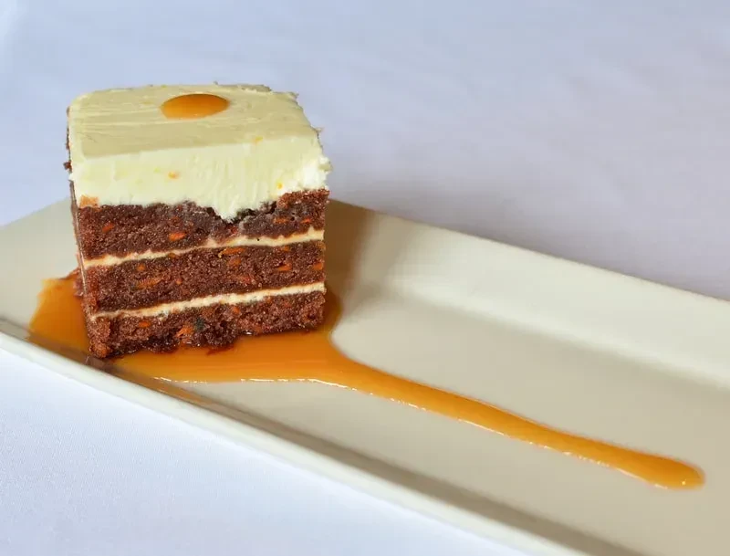 Carrot cake slice with cream cheese frosting, amber topping and drizzle.