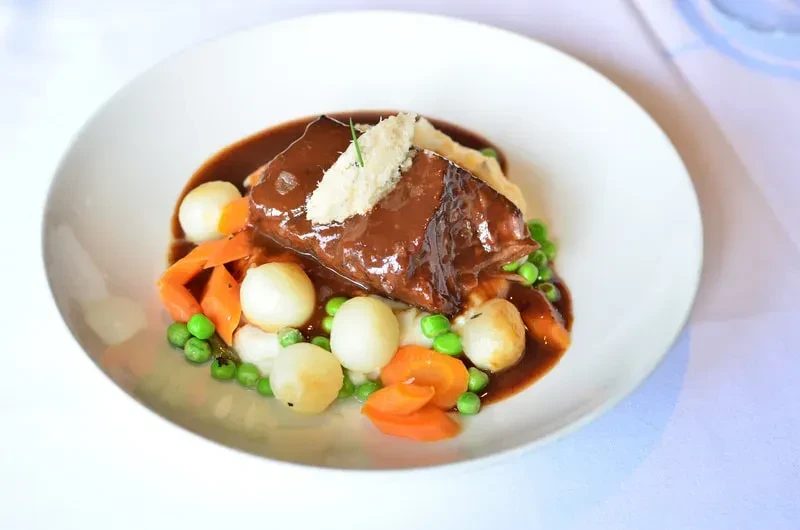 Professionally plated braised meat, mashed potatoes, gravy, and vegetables.