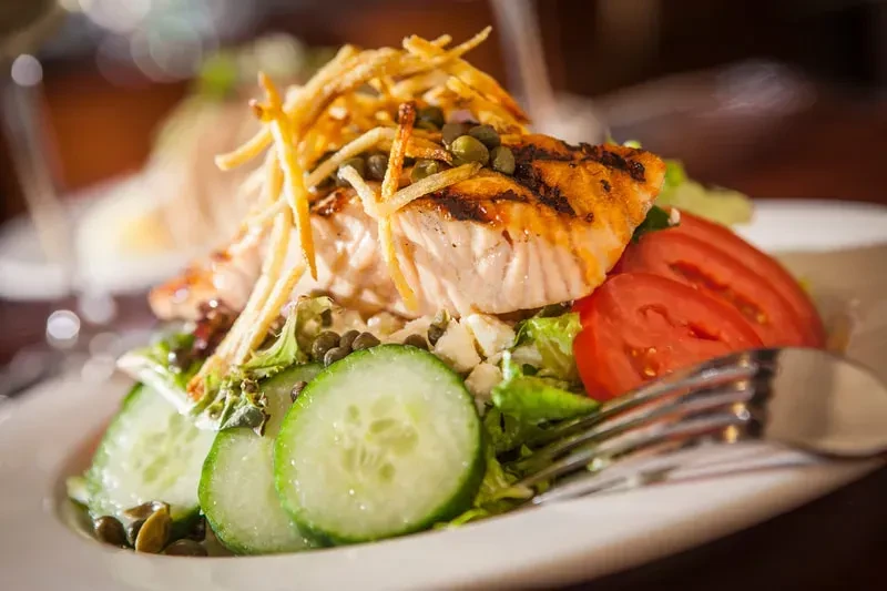 Close-up of grilled salmon salad with vegetables, feta, and char marks.