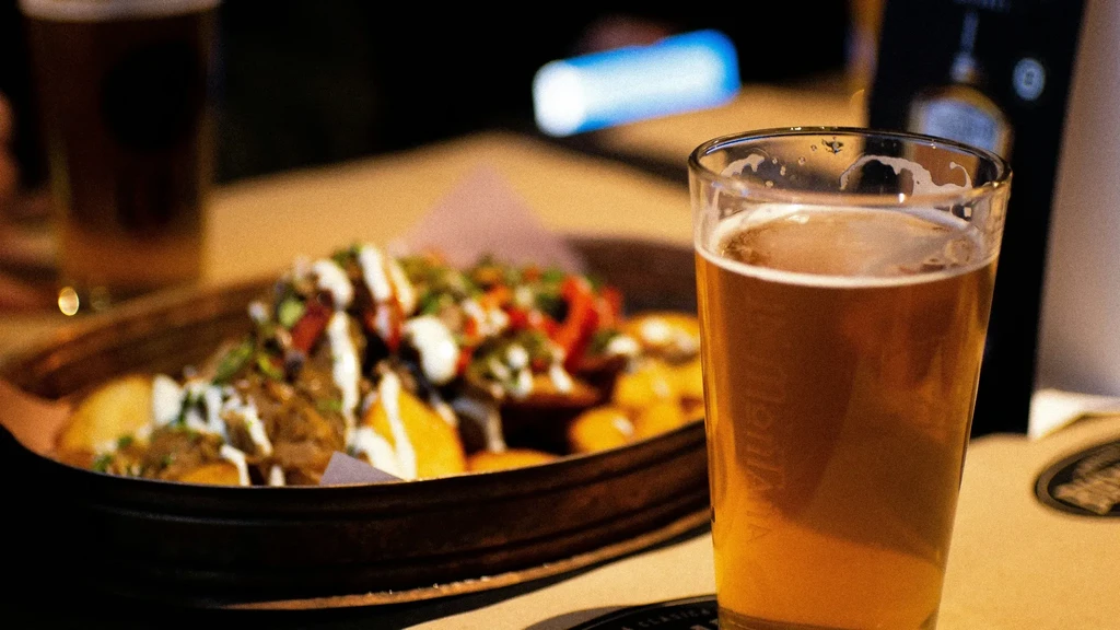 Sharp amber beer, blurred nachos, and another beer in dim light.