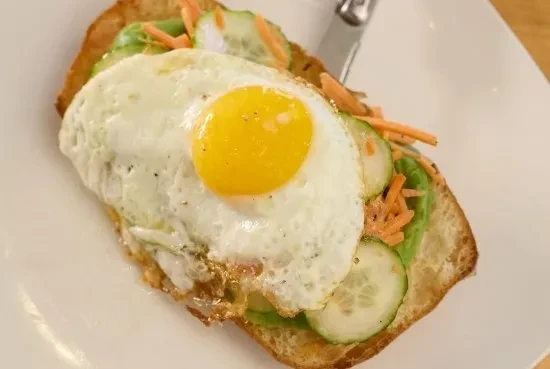 Toasted bread with fried egg, avocado, cucumber, and shredded carrots.