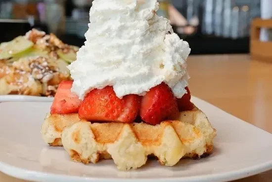 Close-up of a golden-brown waffle with strawberries and whipped cream.