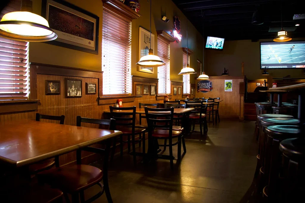 Casual sports bar interior with warm lighting, TVs, neon signs, Ohio State art.