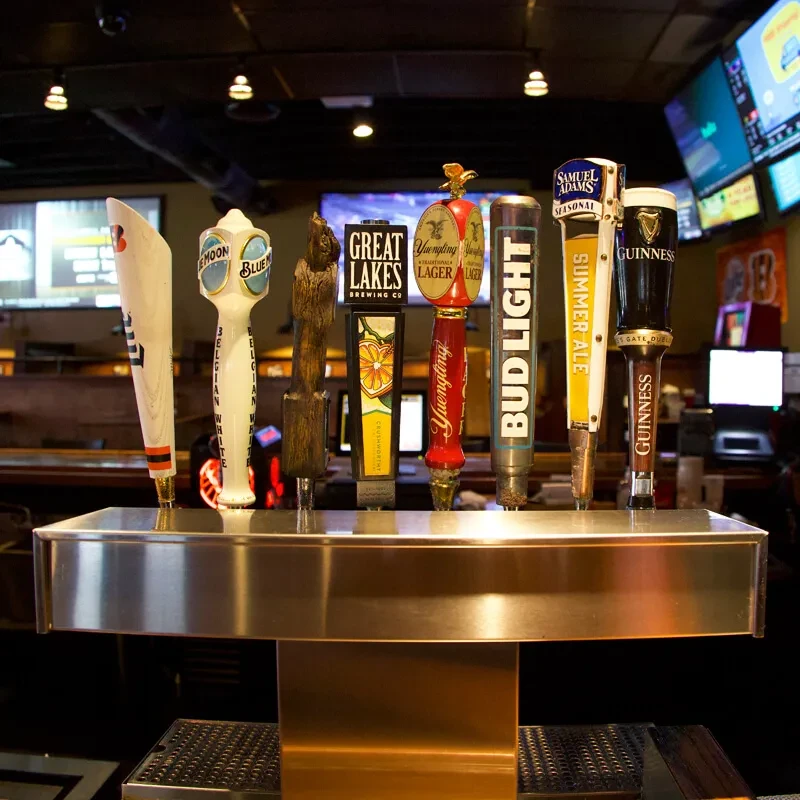 Eight distinct beer tap handles on a stainless steel draft system.