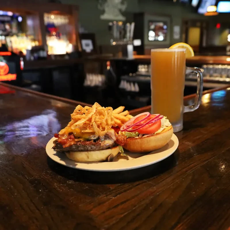Close-up of a stacked burger, fries, onion rings, and a beer.