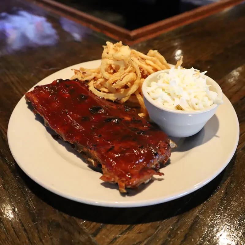 Close-up of barbecued ribs, golden onion rings, and white coleslaw.