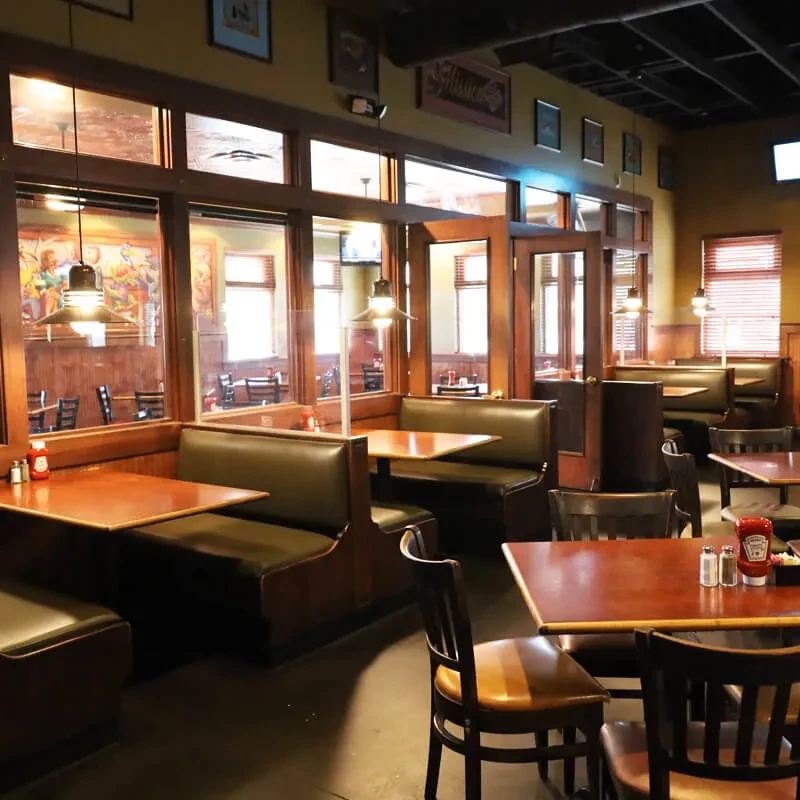 Empty casual restaurant interior with green booths, wooden tables, warm lighting.