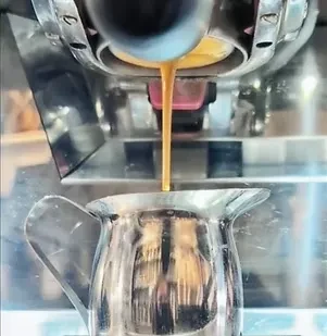 Espresso machine dispensing rich, golden-brown coffee into a metal pitcher.