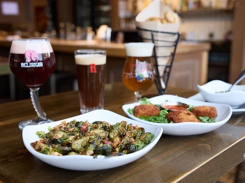 Roasted Brussels sprouts, breaded appetizers, fries, and three beers on dark wood.
