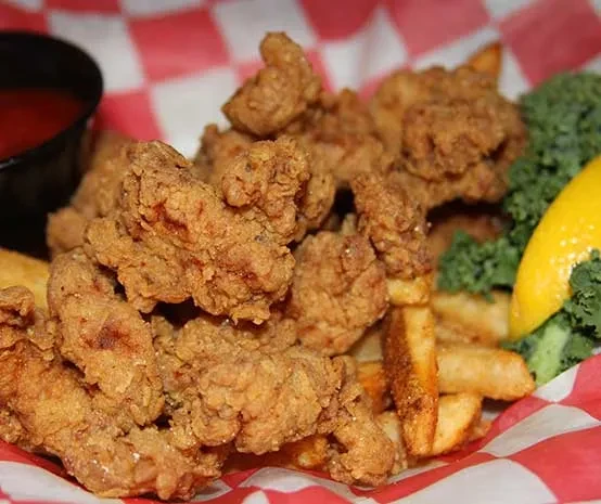 Basket of deep-fried food and fries with sauce, lemon, and garnish.