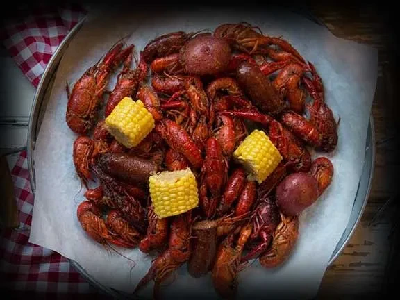 Overhead seafood boil: bright red crawfish, corn, potatoes, and sausage.