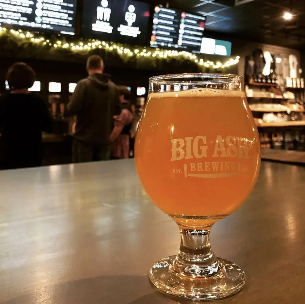 Big Ash Brewing amber beer glass on a bar, blurred background.