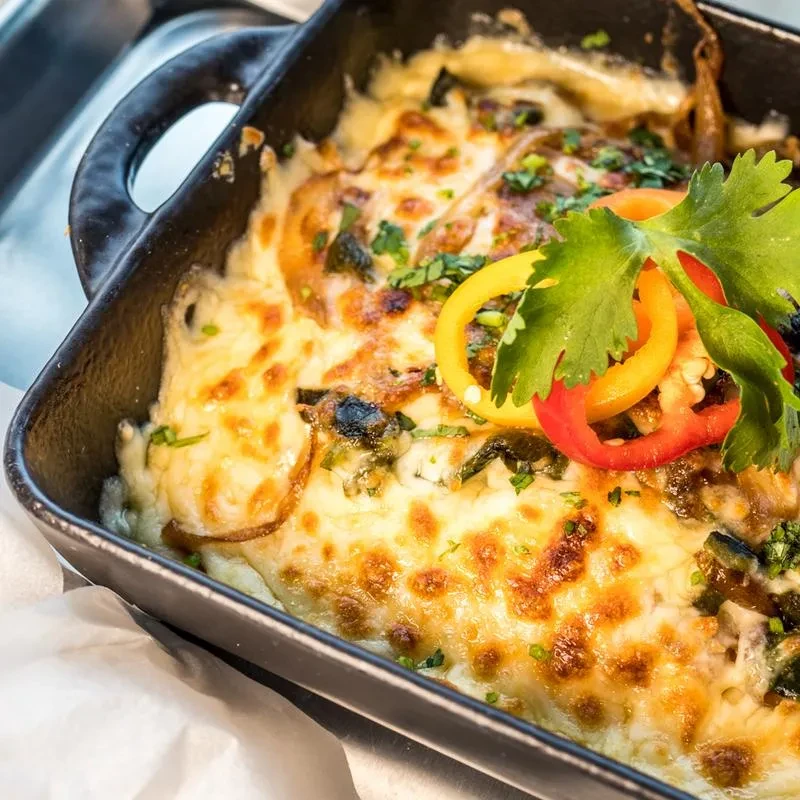 Close-up of bubbling cheesy baked casserole with herbs and bell peppers.