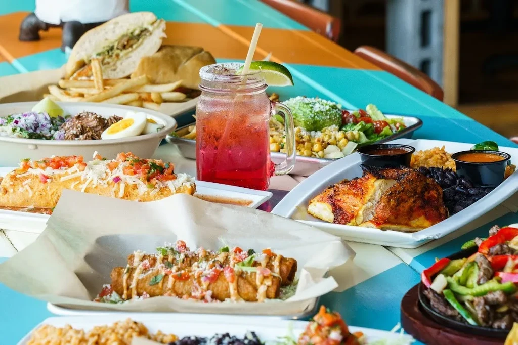 Colorful table spread with fajitas, tacos, grilled chicken, and a red cocktail.