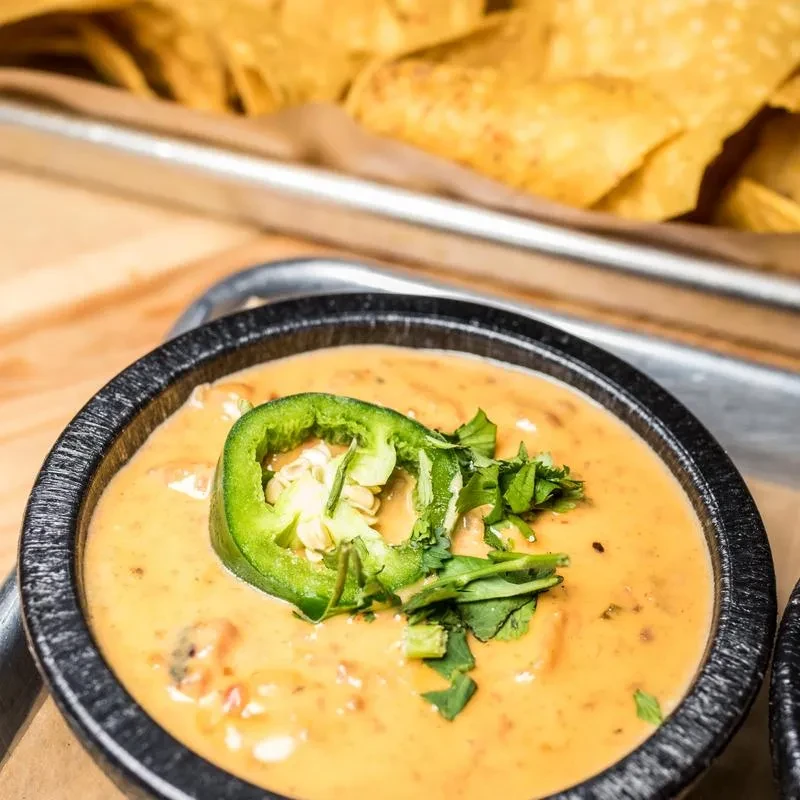 Golden-orange queso in a dark bowl with jalapeño and cilantro.