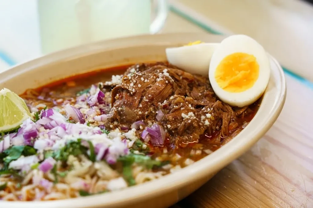 Dark meat stew with cheese, onions, cilantro, hard-boiled egg, and lime.