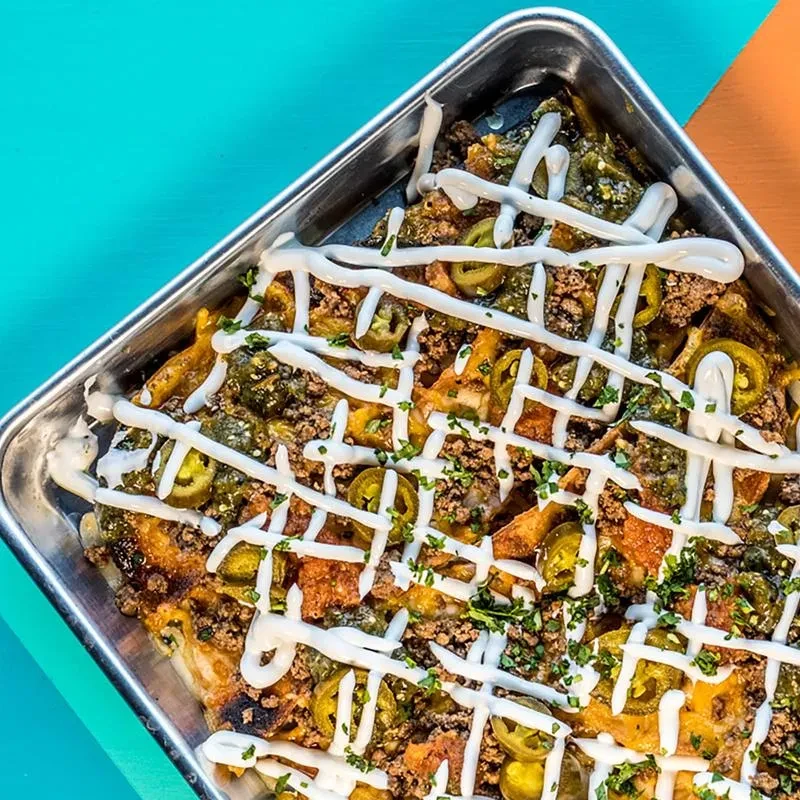 Nachos in metal tray, topped with meat, jalapeños, and sour cream.