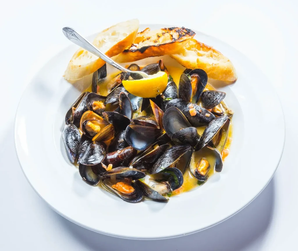 Steamed mussels in yellow broth with grilled baguette and lemon.