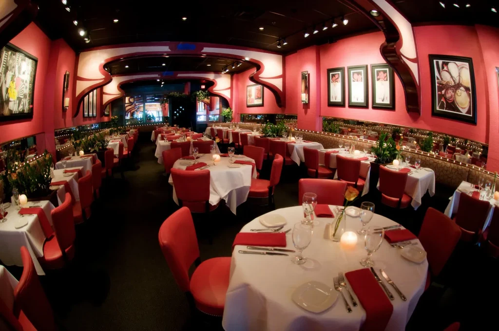 Empty restaurant interior with red walls, white tables, and lit candles.