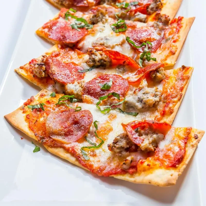 Thin-crust flatbread pizza slices with pepperoni, sausage, cheese, and herbs.