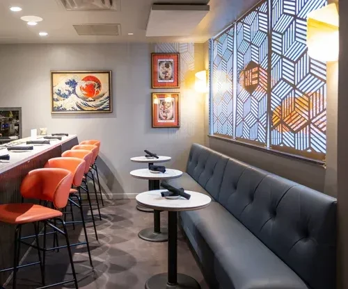 Modern restaurant interior with a bar, orange stools, and grey booth.